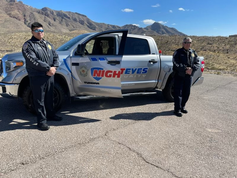 Two Night Eyes guards standing in front of a Night Eyes silver truck in El Paso.